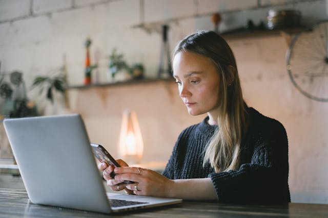 serious woman browsing smartphone near laptop